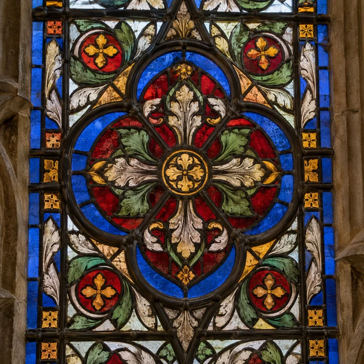 Nahaufnahme eines farbintensiven Glasfensters mit Blumenmotiven, dunklen Bleiruten und verwitterter Steinfassung
